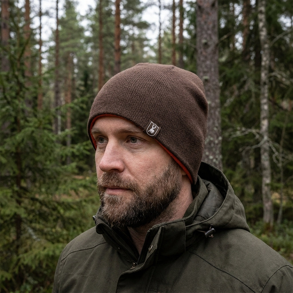 Man wearing a brown beanie and green jacket in a forest setting